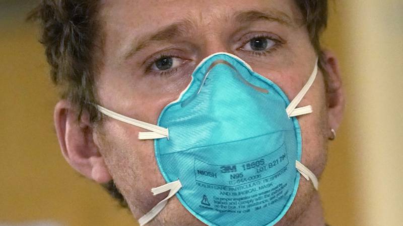 Registered nurse Scott McGieson wears an N95 mask as he walks out of a patient's room in the...